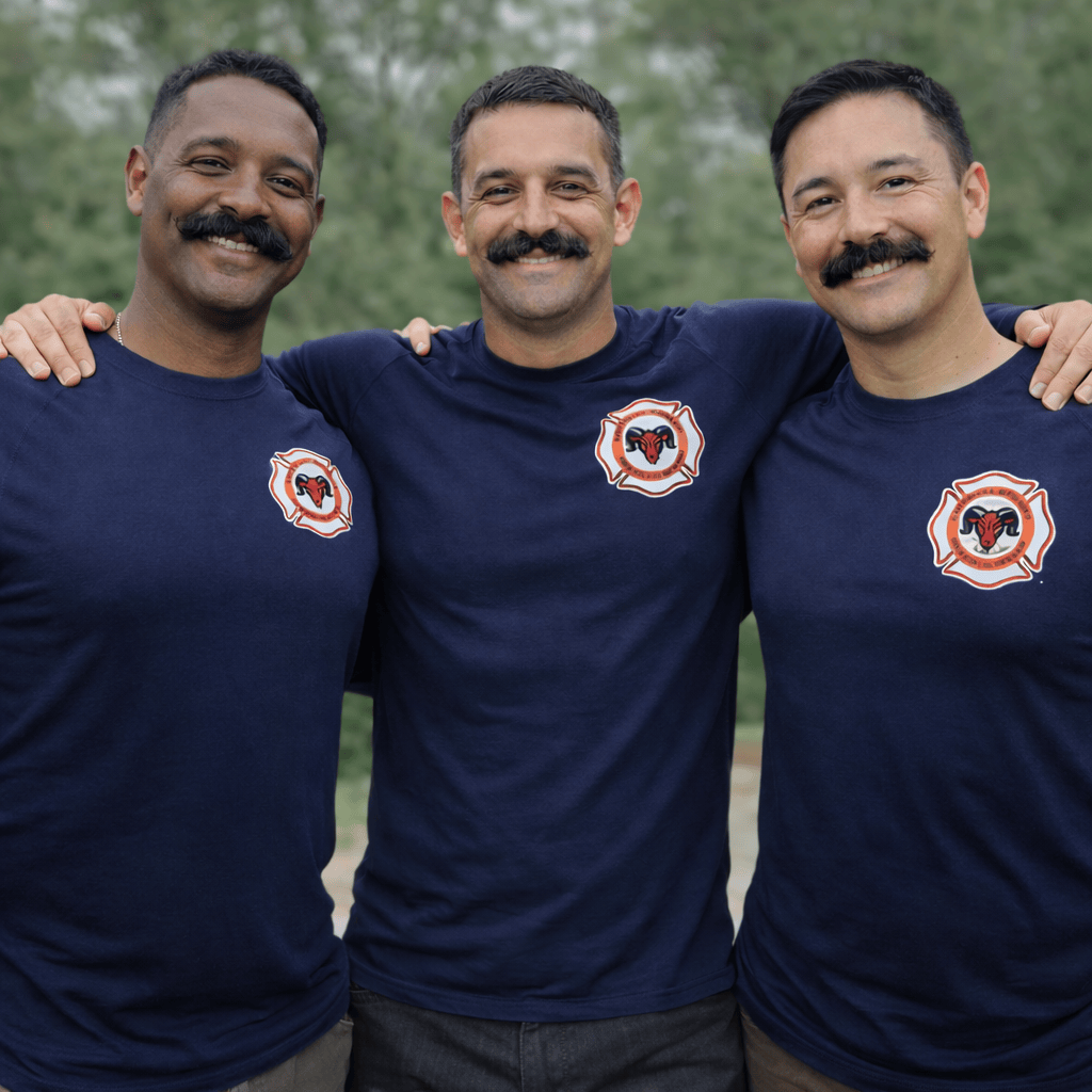 Three smiling first responders wearing navy Armadillo Woolery performance shirts outdoors, representing firefighter-founded apparel built for teamwork, comfort, and long-shift durability.