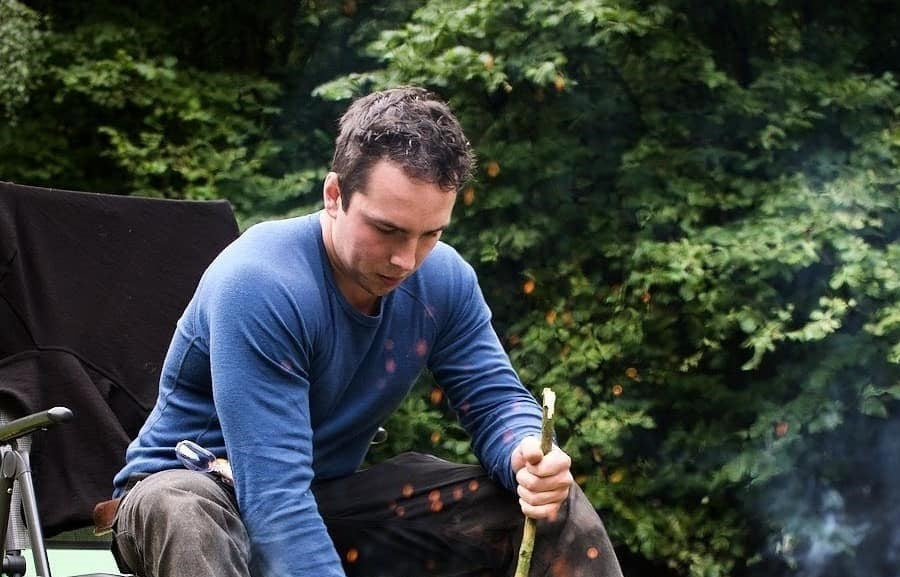 Man sitting around a campfire in his Panther shirt.